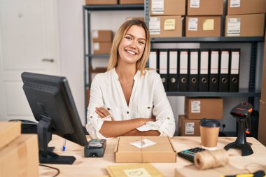Young blonde woman working at small business ecommerce happy face smiling with crossed arms looking at the camera. positive person. 