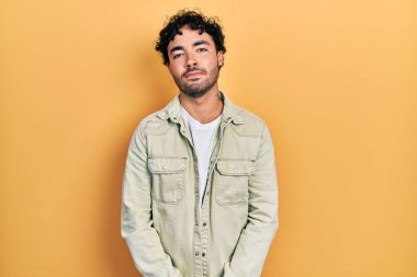 Günlük kıyafetler giyen genç İspanyol adam yüzünde ciddi bir ifadeyle rahatlamış. Basit ve doğal bir şekilde kameraya bakıyorsun.. 