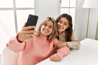 Genç çift mutlu bir şekilde gülümsüyor. Evdeki akıllı telefonun yanında selfie çekiyorlar..