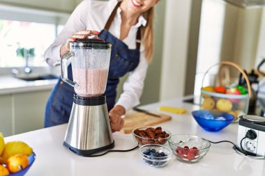 Genç sarışın kadın gülümsüyor. Kendine güveni tam. Smoothie 'yi sıvılaştırıyor.