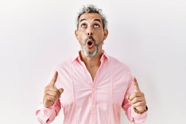 Orta yaşlı, ispanyol kökenli bir adam şaşırmış ve şaşırmış bir şekilde yukarı bakıyor ve parmaklarını gösterip kollarını kaldırıyor.. 