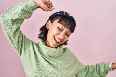 Genç, güzel bir kadın pembe arka planda dans ediyor mutlu ve neşeli, gülümseyen hareketli ve kendinden emin müzik dinliyor. 