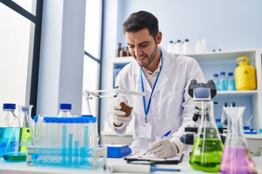 Genç İspanyol bilim adamı elinde değerli taşla laboratuardaki belgeye yazı yazıyor.