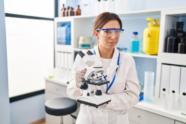 Genç esmer kadın mikroskopta çalışan şüpheci ve gergin bir bilim adamı sorun yüzünden surat asıyor. negatif kişi. 