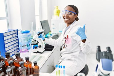 African woman working at scientist laboratory smiling happy and positive, thumb up doing excellent and approval sign 