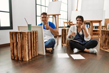 Sanat stüdyosundaki genç İspanyol çift mutlu ve pozitif gülümsüyor, başparmağıyla mükemmel ve onay işareti yapıyor. 