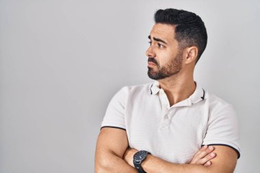 Young hispanic man with beard wearing casual clothes over white background looking to the side with arms crossed convinced and confident 