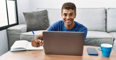 Genç İspanyol adam evde dizüstü bilgisayarla ders çalışıyor.