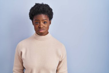 Afro-Amerikalı bir kadın mavi arka planda durmuş komik suratıyla yanaklarını şişiriyor. Havayla şişmiş ağız, çılgın bir ifade.. 