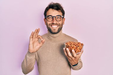 Fıstık sakallı yakışıklı adam parmaklarıyla imza atıyor, gülümsüyor ve mükemmel bir sembol oluşturuyor. 