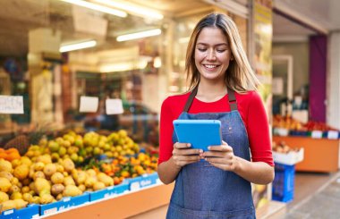 Young hispanic woman shop assistant using touchpad at fruit market