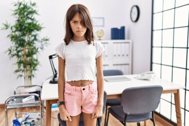 Young hispanic girl standing at pediatrician clinic skeptic and nervous, frowning upset because of problem. negative person. 