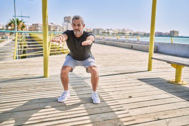 Orta yaşlı İspanyol adam deniz kenarında spor kıyafeti giyiyor.