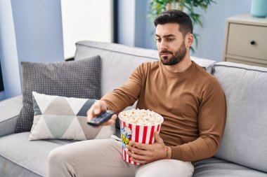 Evdeki kanepede oturup film izleyen sıkıcı İspanyol genç adam.