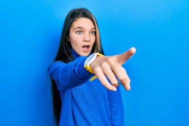 Young brunette girl wearing turtleneck sweater pointing with finger surprised ahead, open mouth amazed expression, something on the front 