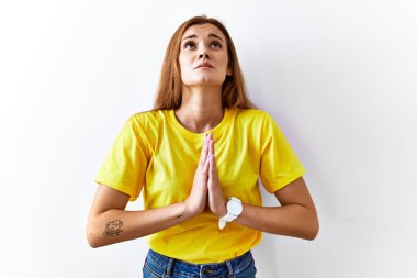 Genç esmer kadın izole edilmiş arka planda duruyor. Elleriyle yalvarıyor ve dua ediyor. Yüzünde umut ifadesi var. Yalvarıyor. 