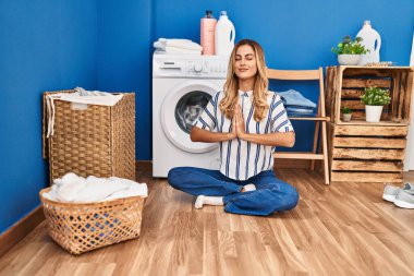 Genç sarışın kadın yoga yapıyor çamaşır odasında çamaşır makinesini bekliyor.