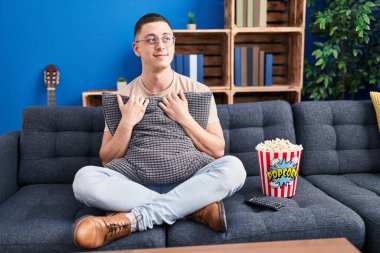 Young man eating popcorn smiling looking to the side and staring away thinking. 