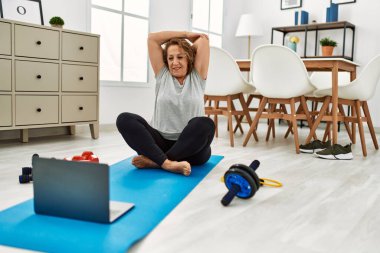 Orta yaşlı, beyaz bir kadın evinde dizüstü bilgisayar kullanarak gülümsüyor.