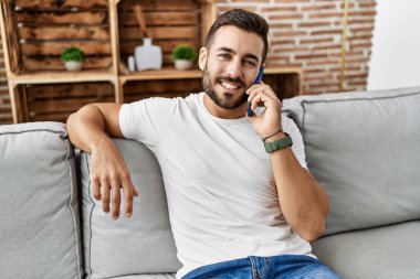 Young hispanic man smiling confident talking on the smartphone at home