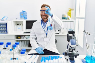 Middle age man working at scientist laboratory smiling happy doing ok sign with hand on eye looking through fingers 