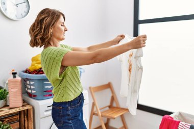 Orta yaşlı İspanyol kadın çamaşırhanede kirli tişört tutuyor.