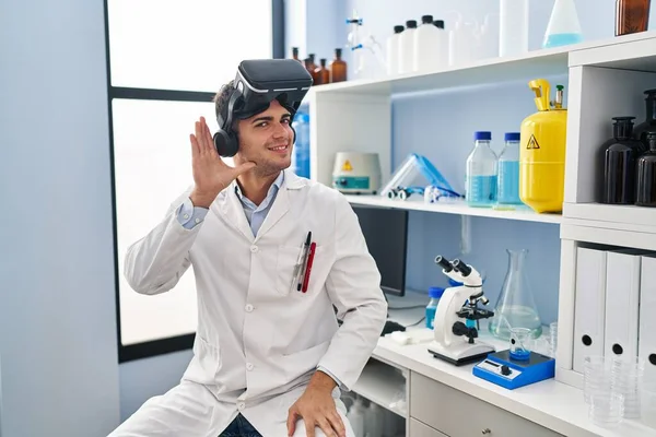 科学研究所で働いている若いヒスパニック系の男性は 耳を傾け 噂やゴシップに耳を傾けながら手で笑顔Vrの眼鏡をかけています 聴覚障害の概念 — ストック写真