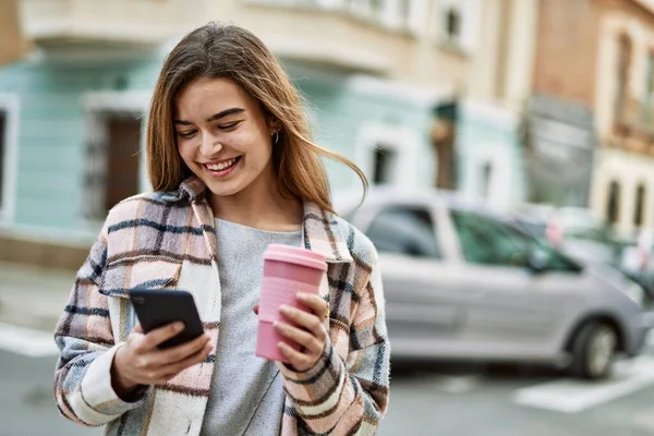 Genç Sarışın Kadın Gülümsüyor Akıllı Telefon Kullanıyor Sokakta Kahve Tutuyor — Stok fotoğraf