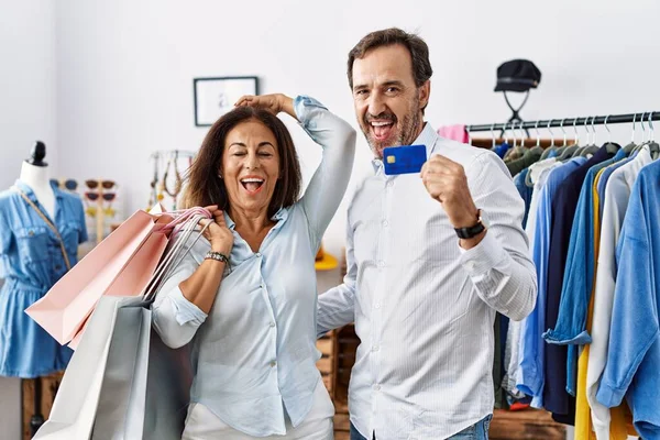 Hispanic middle age couple holding shopping bags and credit card smiling confident touching hair with hand up gesture, posing attractive and fashionable 