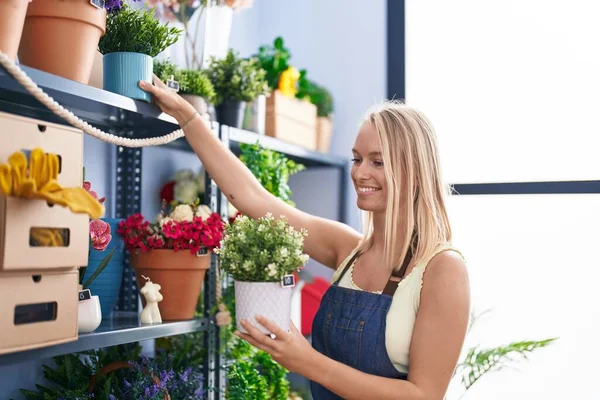 Çiçekçide çiçek tutan, gülümseyen genç sarışın kadın.