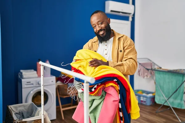 Joven Afroamericano Hombre Sonriendo Confiado Sosteniendo Ropa Sala Lavandería — Foto de Stock