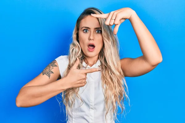 Beautiful young blonde woman doing picture frame gesture with hands afraid and shocked with surprise and amazed expression, fear and excited face.