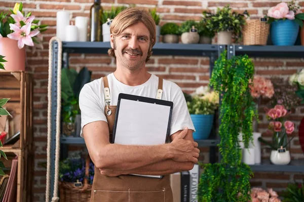 Young blond man florist smiling confident holding clipboard at flower shop