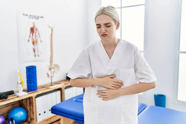 Young caucasian woman working at pain recovery clinic with hand on stomach because indigestion, painful illness feeling unwell. ache concept.