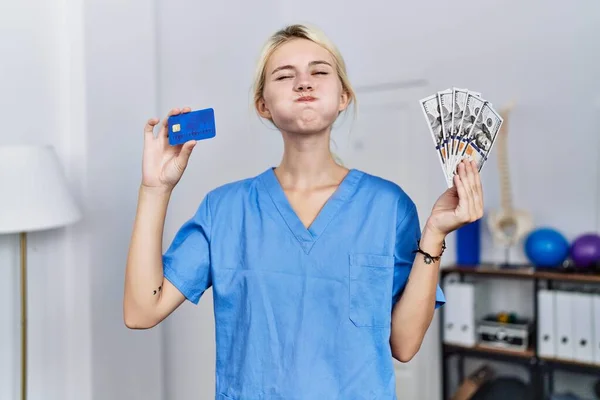 Mulher Fisioterapeuta Jovem Segurando Cartão Crédito Notas Dólares Soprando Bochechas — Fotografia de Stock