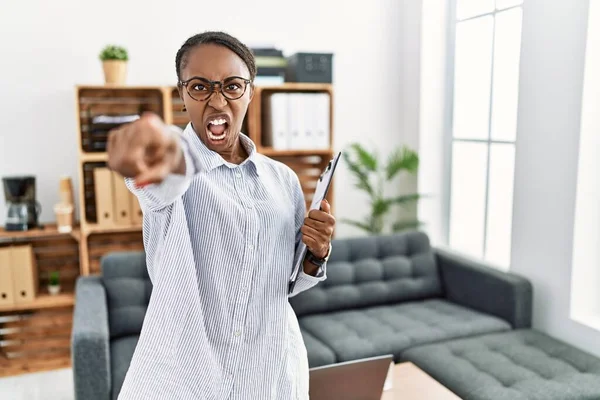 African woman working at psychology clinic pointing displeased and frustrated to the camera, angry and furious with you