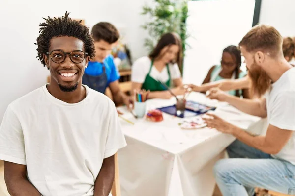 Group of people drawing sitting on the table. African american man smiling happy looking to the camera at art studio.