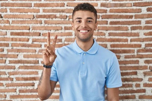 巴西年轻人站在砖墙上 用2号手指指指指点点 面带微笑 自信而快乐 — 图库照片