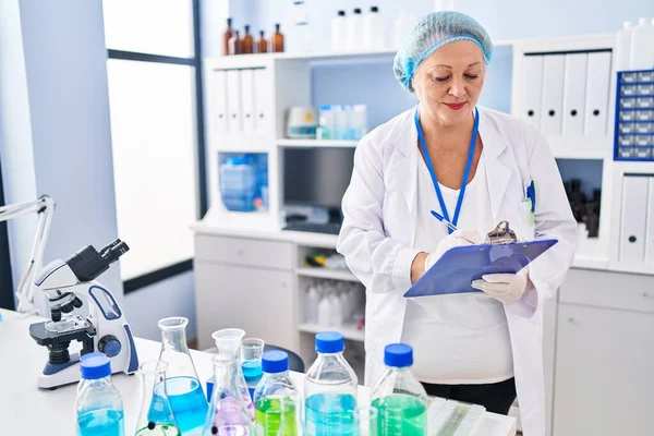 Middle Age Blonde Woman Wearing Scientist Uniform Writing Clipboard Laboratory — Stock fotografie