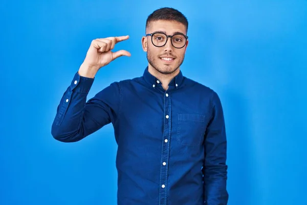 Mladý Hispánec Brýlích Modrém Pozadí Úsměvem Sebevědomým Gestem Rukou Který — Stock fotografie