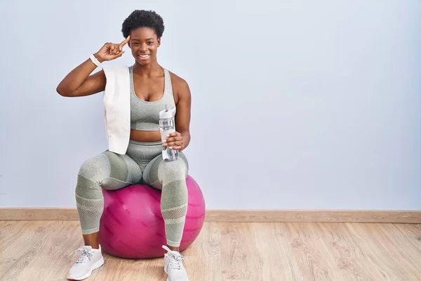 African american woman wearing sportswear sitting on pilates ball smiling pointing to head with one finger, great idea or thought, good memory