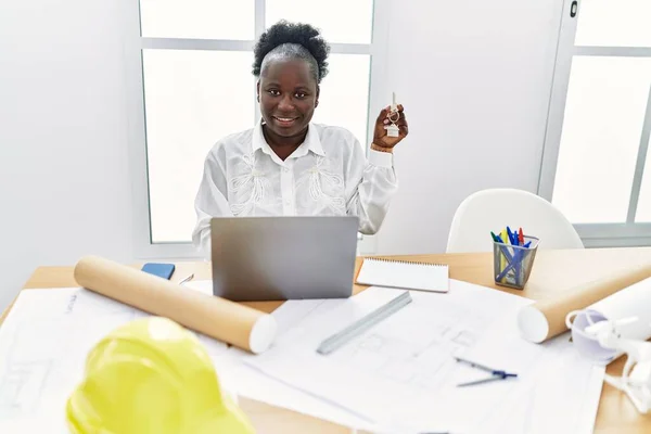 家の鍵を持っている建築スタジオで働いている若いアフリカの女性は ポジティブで幸せな立ち姿で 自信を持って笑顔で歯を見せています — ストック写真