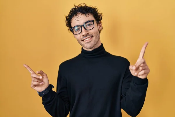 站在黄色背景上的西班牙裔男子自信地微笑着 用手指指向不同的方向 复制广告空间 — 图库照片