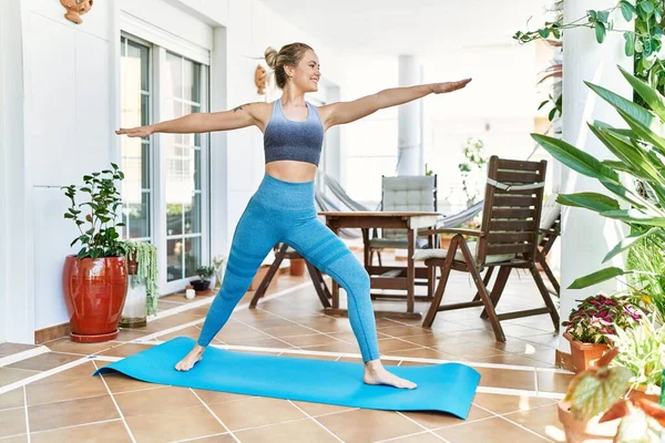 Beautiful caucasian woman training and stretching at the terrace at her home. Doing asana and wellbeing work out on yoga mat.