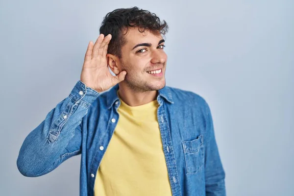 Jovem Hispânico Sobre Fundo Azul Sorrindo Com Mão Sobre Ouvido — Fotografia de Stock