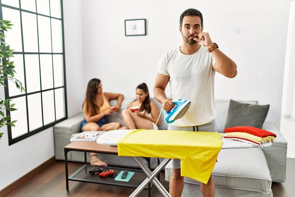 Genç İspanyol adam evde ütü yapıyor ve dudakları parmaklarıyla fermuar gibi kapalı. gizli ve sessiz, tabu konuşması 