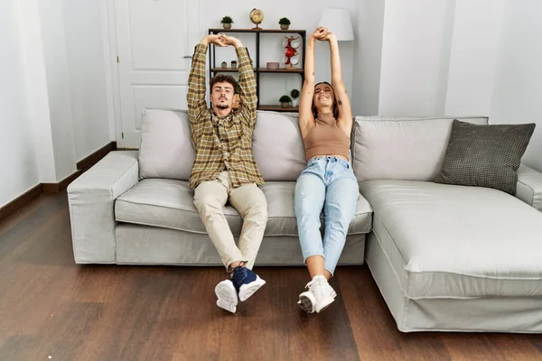 Young Hispanic Couple Relaxed Stretching Arms Sitting Sofa Home — Stockfoto
