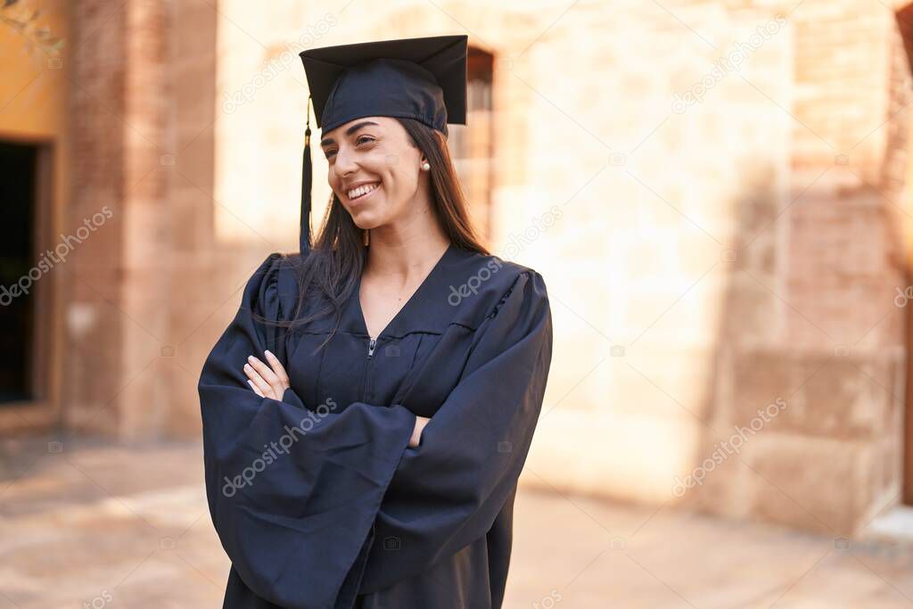 Young hispanic woman wearing graduated uniform standing with arms crossed gesture at university