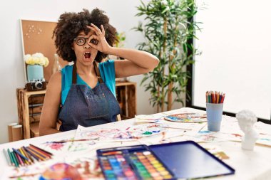 Sanat stüdyosunda afro saçlı güzel bir afro-amerikan kadın. Şaşırmış yüz ifadesiyle şaşırmış, parmaklarından bakan bir jest yapıyor. İnançsız ifade. 