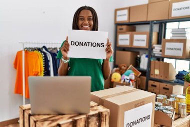Gönüllü üniforma giyen genç Afrikalı Amerikalı kadın yardım merkezinde bağış afişi tutuyor.